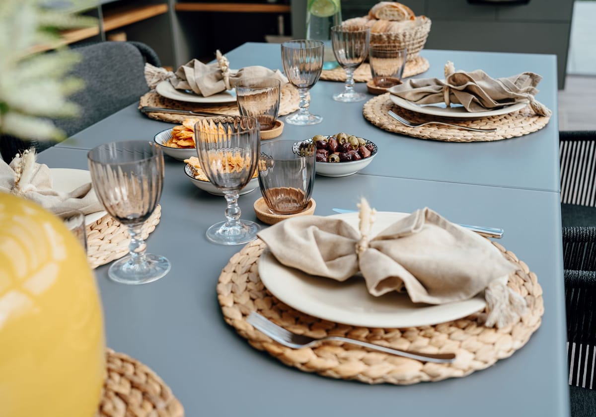 Outdoor dining table set with woven placemats, linen napkins, ribbed glasses, olives and chips