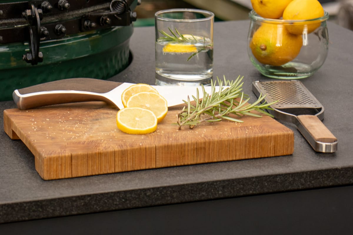 Big Green Egg set into a dark stone island countertop, lemon slices, rosemary and a grater on an end-grain board
