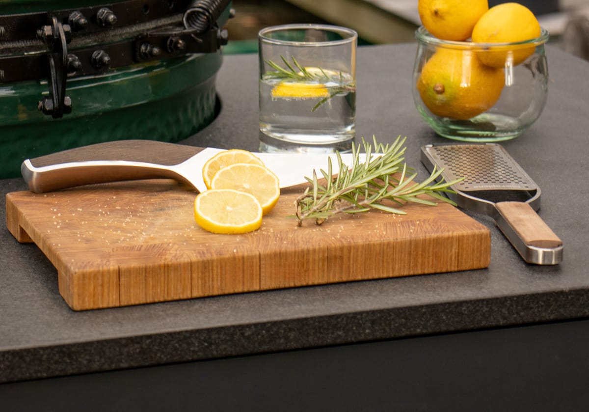 Big Green Egg set into a dark stone island countertop, lemon slices, rosemary and a grater on an end-grain board