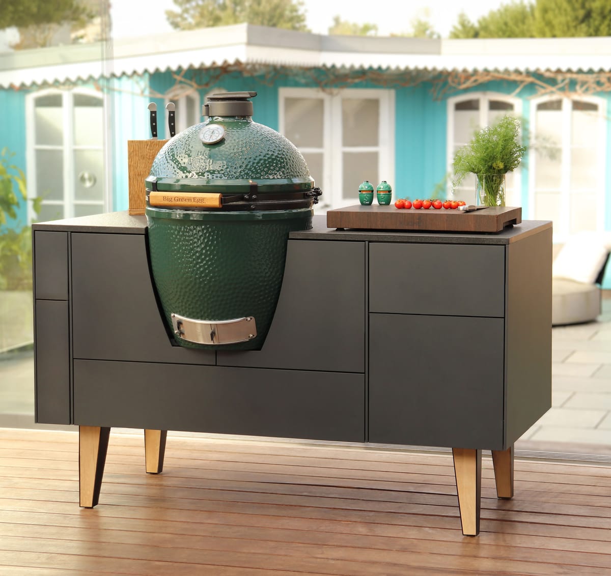 FREILUFT island with anthracite fronts, oak legs and a built-in Big Green Egg on a wooden deck, hanging fireplace