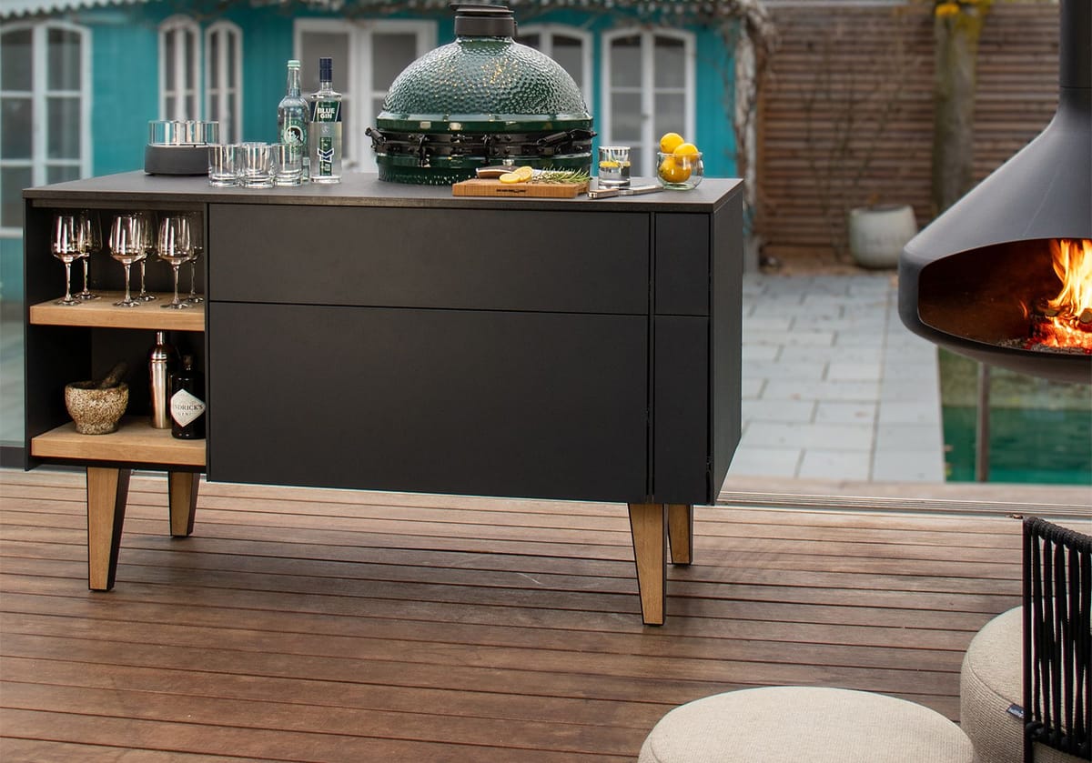Back of an outdoor island with open oak shelves for glasses and bottles, Big Green Egg set into the worktop, poufs on a wood deck
