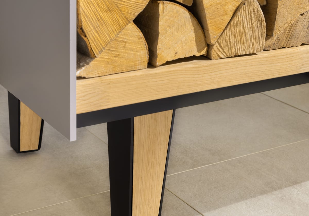 Close-up of a tapered oak and black steel leg under an open firewood shelf of an outdoor island