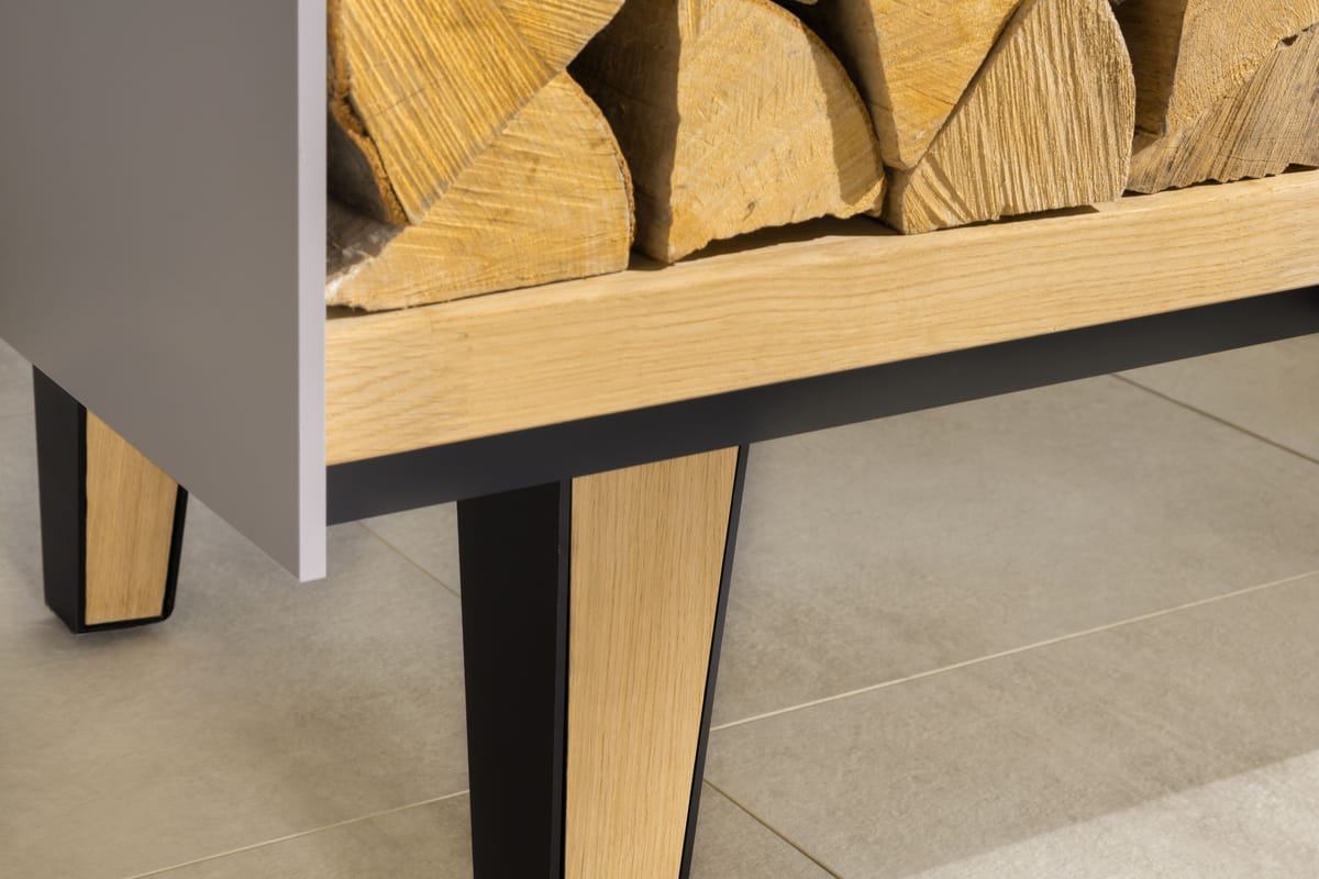 Close-up of a tapered oak and black steel leg under an open firewood shelf of an outdoor island
