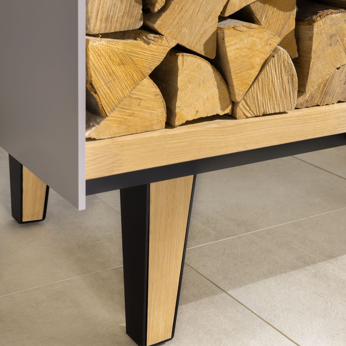 Close-up of a tapered oak and black steel leg under an open firewood shelf of an outdoor island