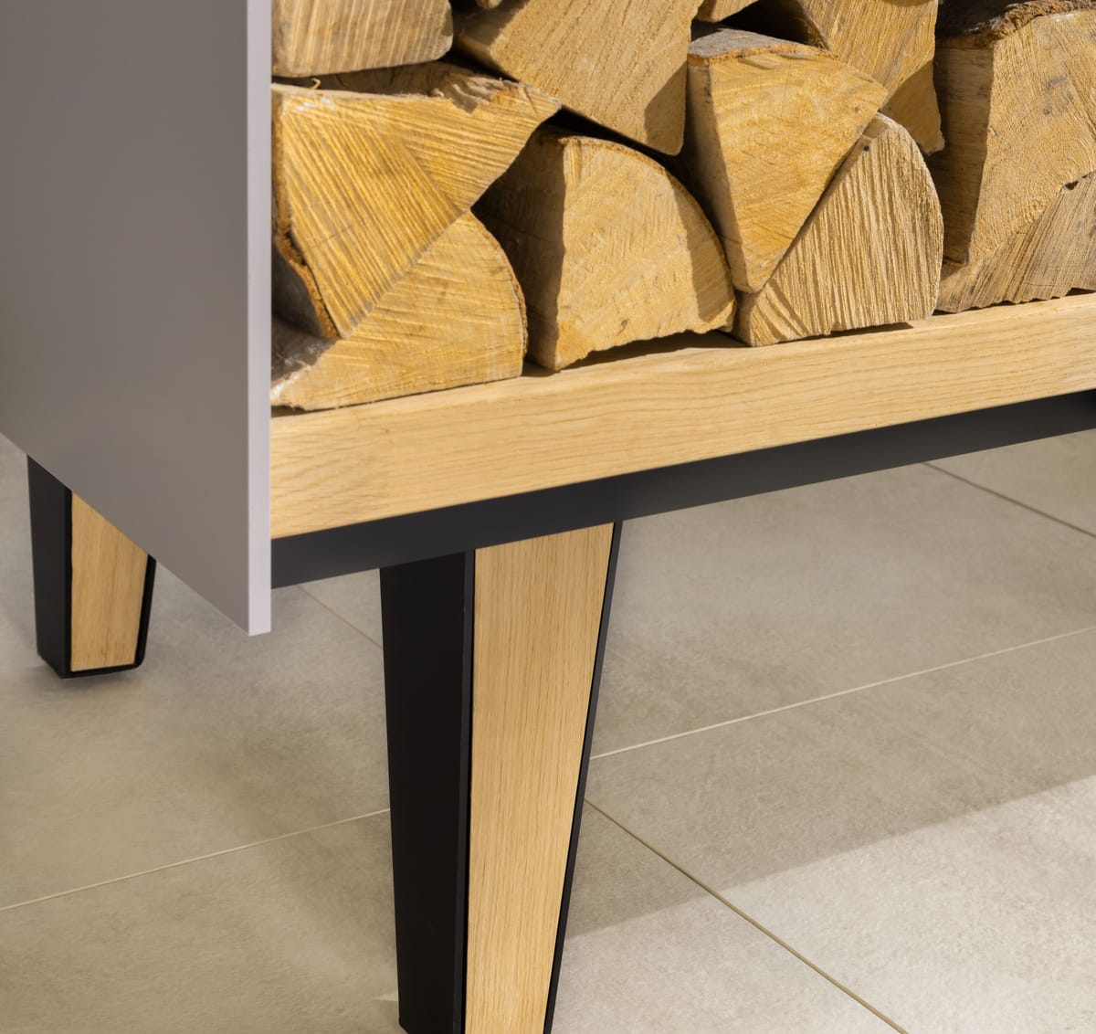 Close-up of a tapered oak and black steel leg under an open firewood shelf of an outdoor island