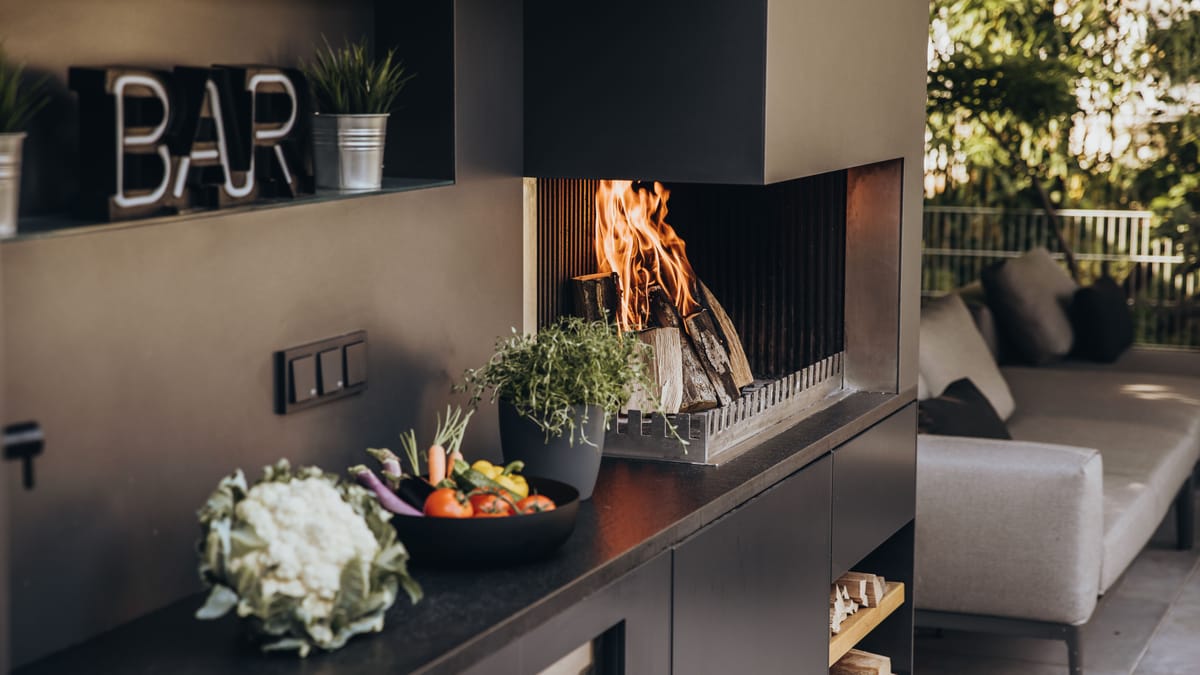 Wood fire in the grill-and-fire element beside herbs and a vegetable bowl on a dark stone counter