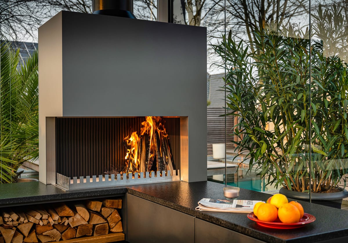 Close-up of a wood fire in the grill-and-fire element above a dark flamed stone countertop with oranges