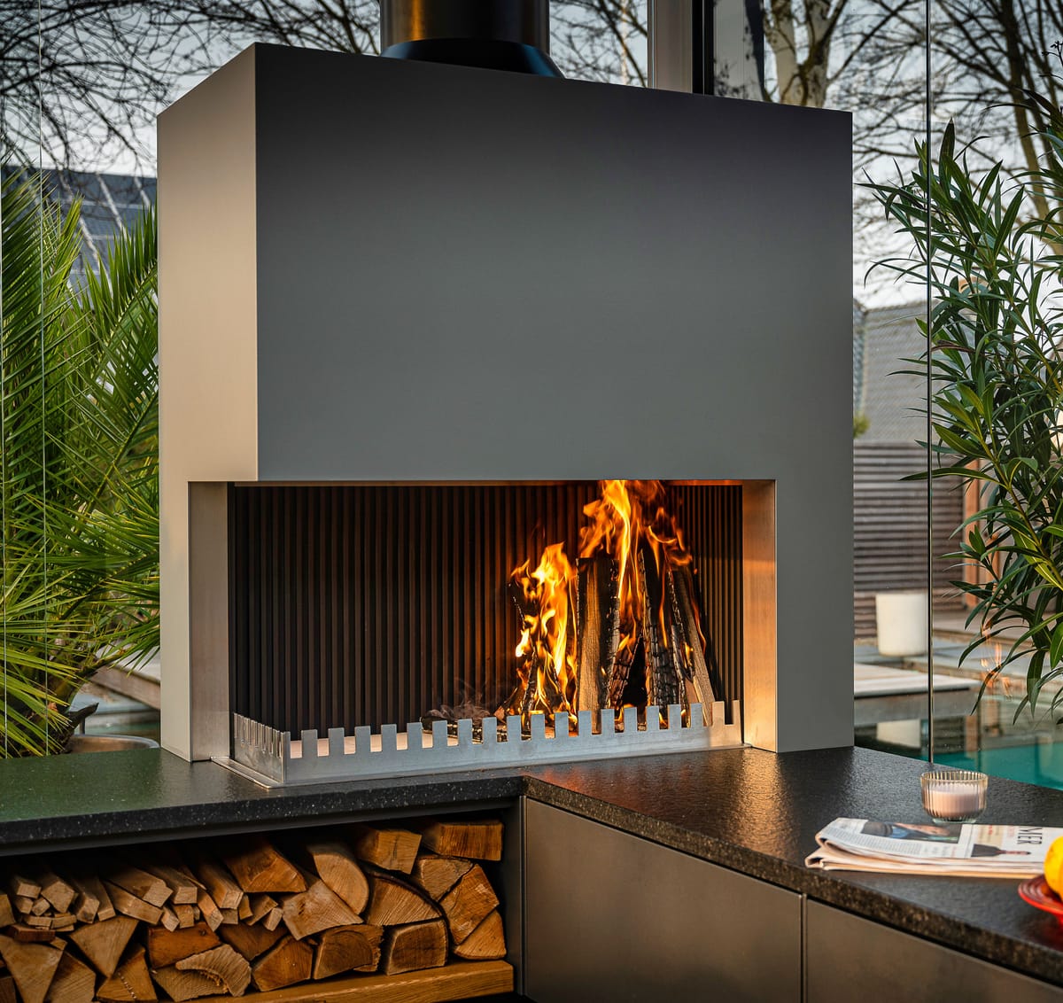 Close-up of a wood fire in the grill-and-fire element above a dark flamed stone countertop with oranges