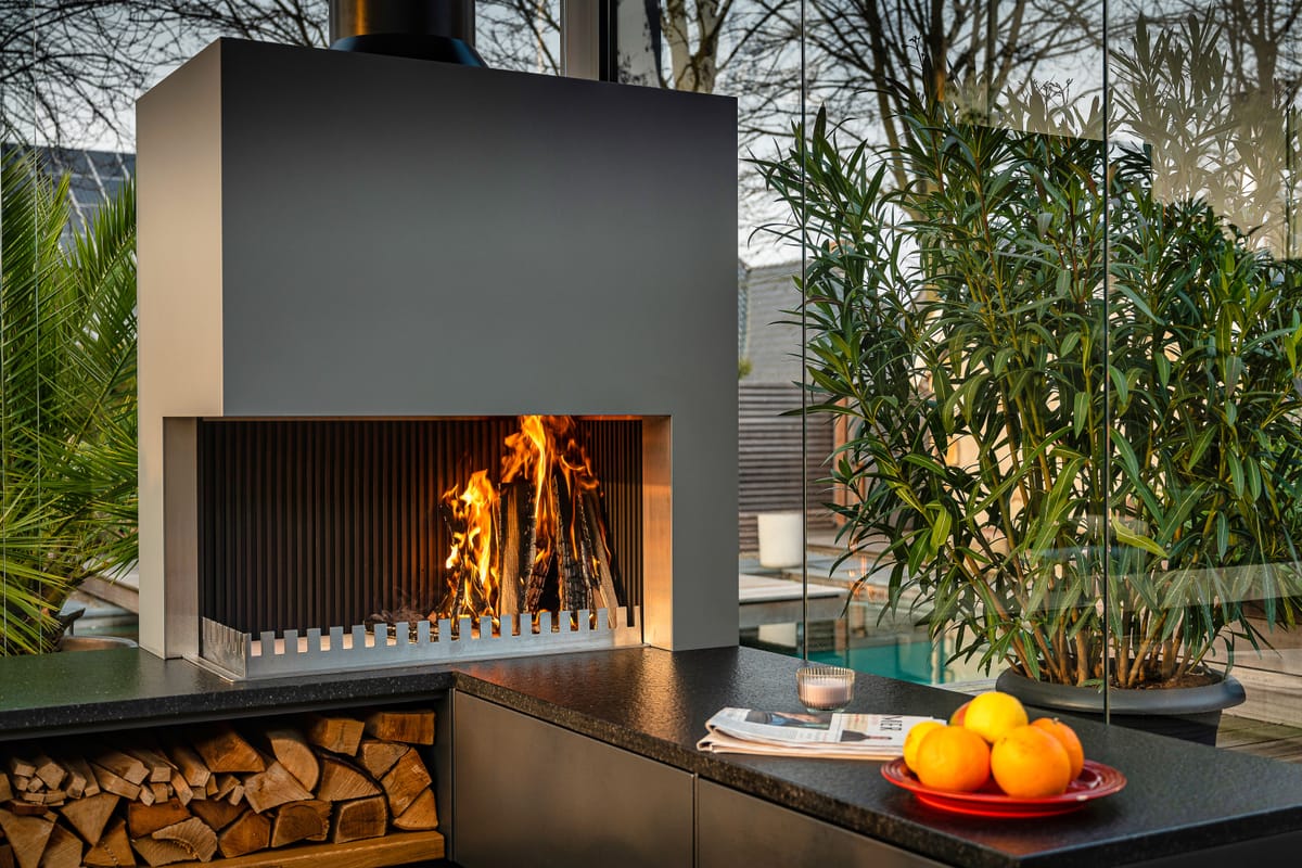 Close-up of a wood fire in the grill-and-fire element above a dark flamed stone countertop with oranges