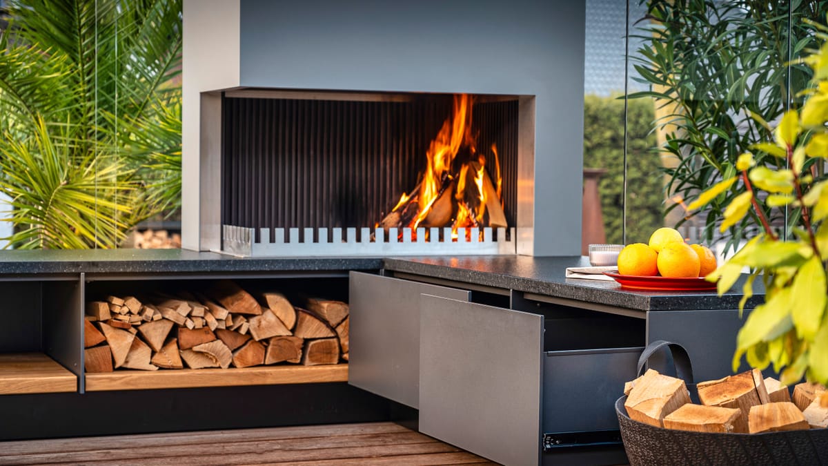 Wood fire in the grill-and-fire element, firewood in an open shelf and a gray drawer pulled open