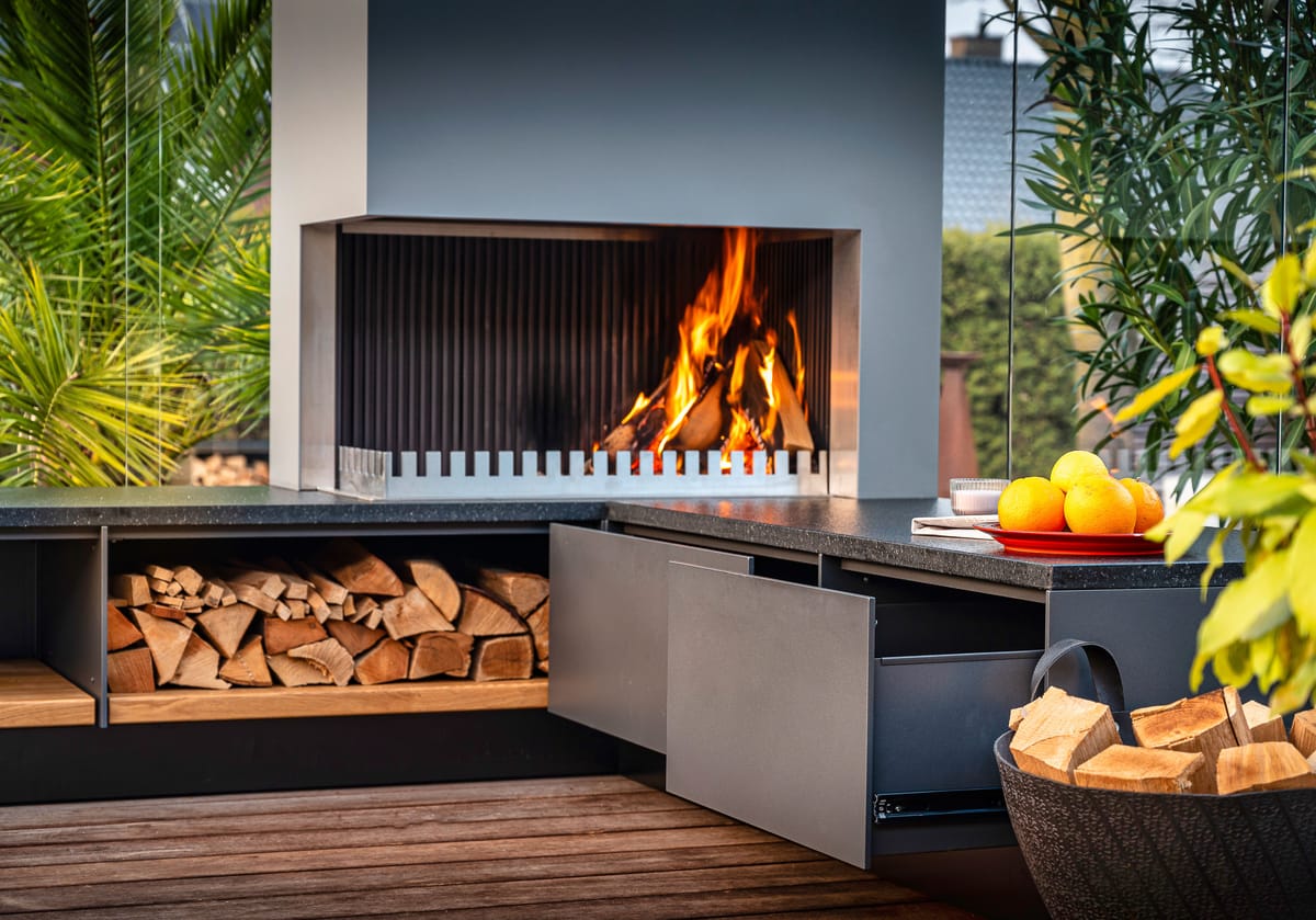 Wood fire in the grill-and-fire element, firewood in an open shelf and a gray drawer pulled open