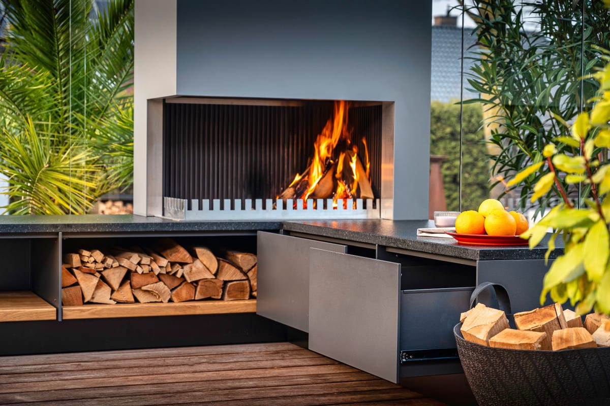 Wood fire in the grill-and-fire element, firewood in an open shelf and a gray drawer pulled open