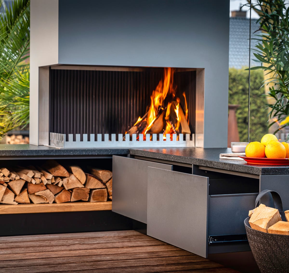 Wood fire in the grill-and-fire element, firewood in an open shelf and a gray drawer pulled open