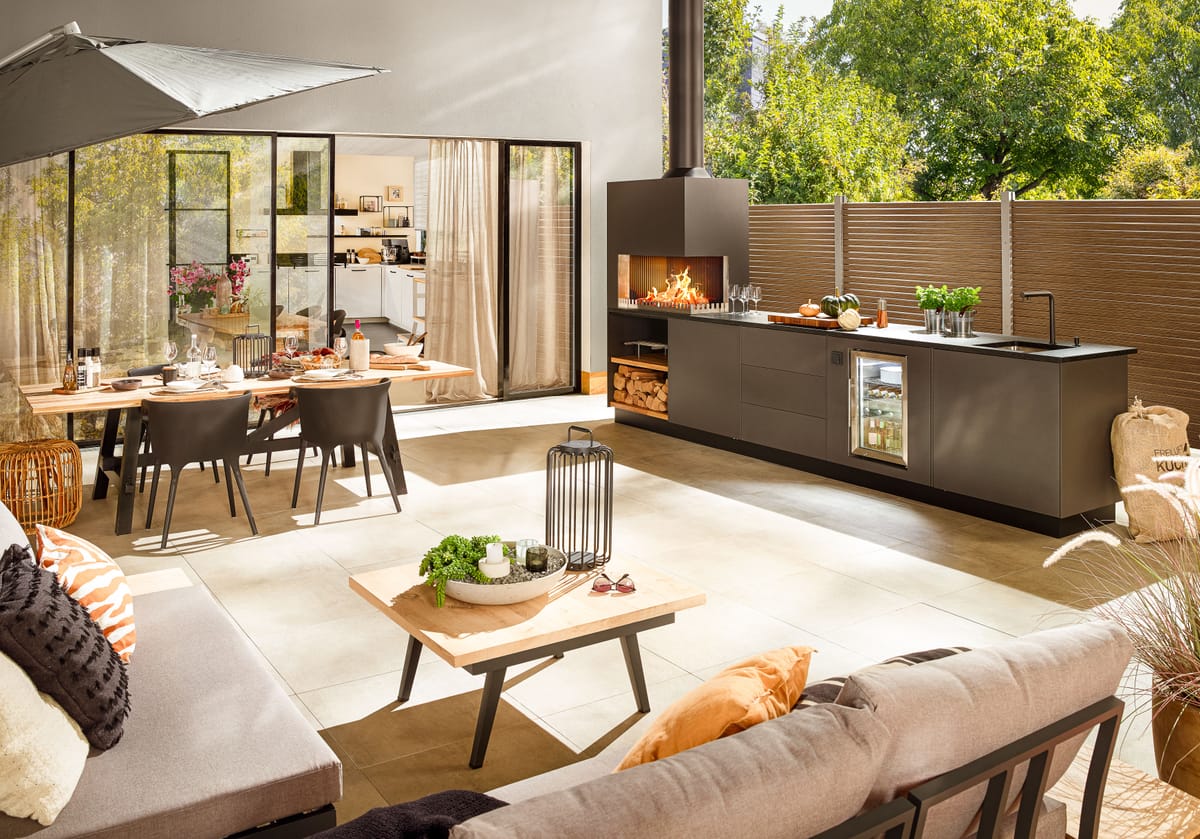 Sunny terrace with lounge, dining table and a dark gray outdoor kitchen with a wood fire and sink