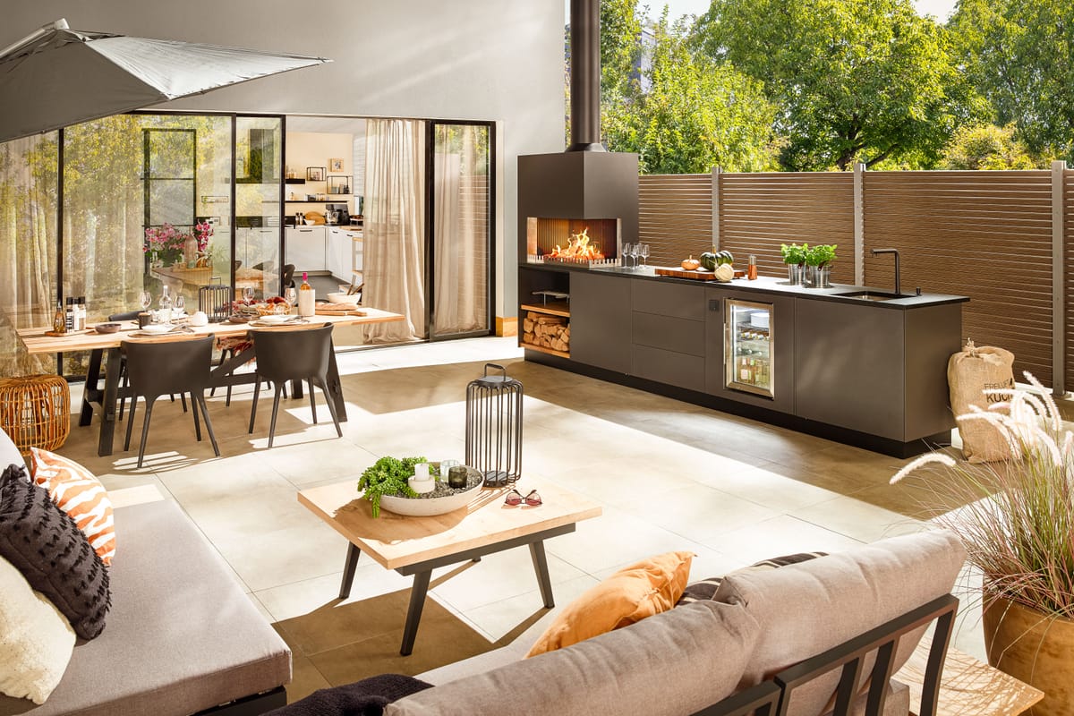 Sunny terrace with lounge, dining table and a dark gray outdoor kitchen with a wood fire and sink