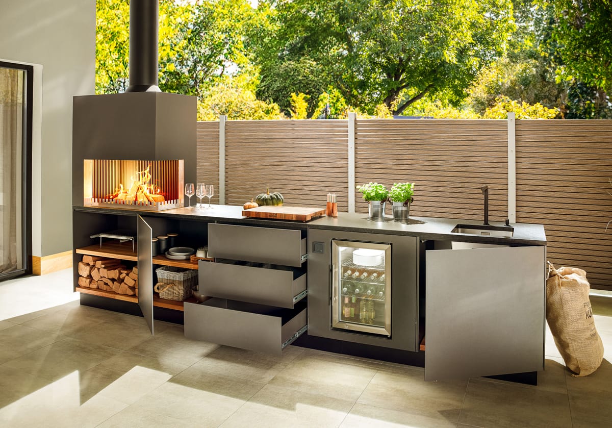Dark gray outdoor kitchen with open drawers and doors, firewood storage, wood fire and glass-door cooler