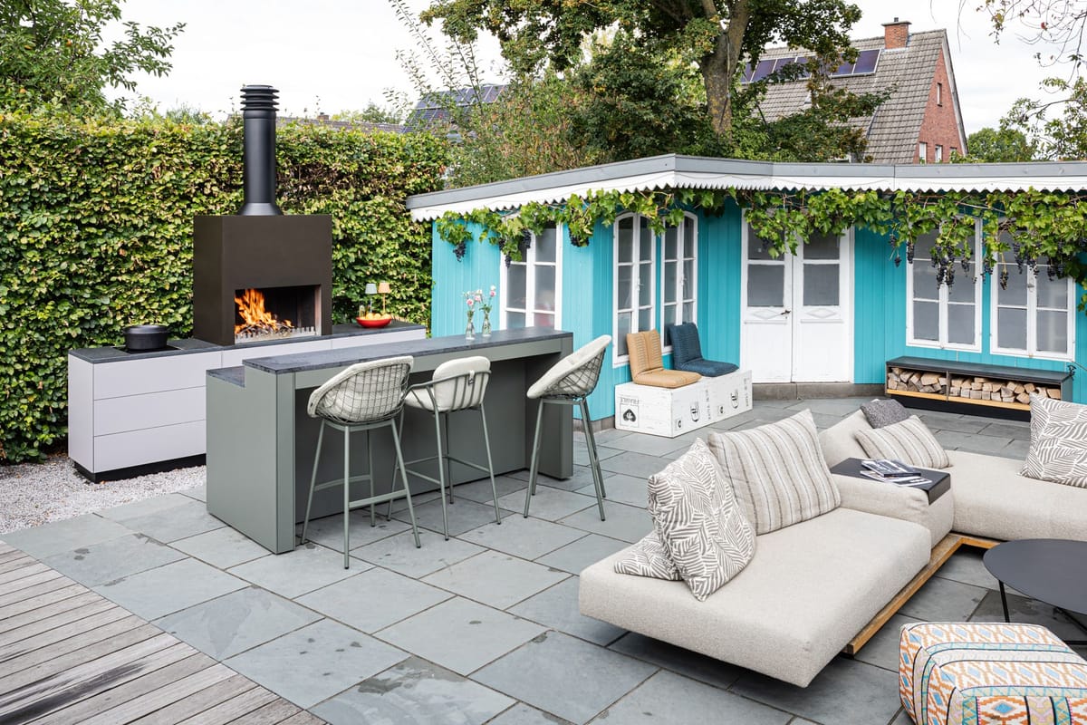 Patio with an outdoor fire hood, light gray kitchen and green bar counter with three stools, turquoise shed behind