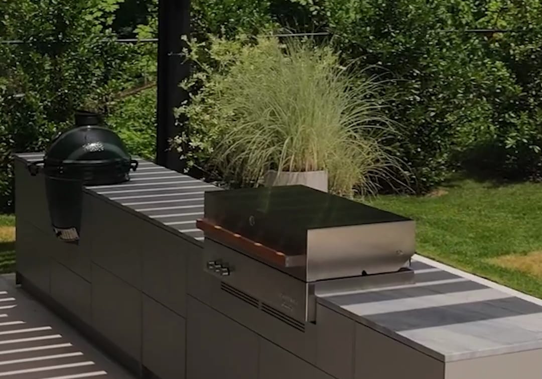 A long gray FREILUFT kitchen run with a Big Green Egg and a built-in grill under a black louvered pergola on Long Island, New York