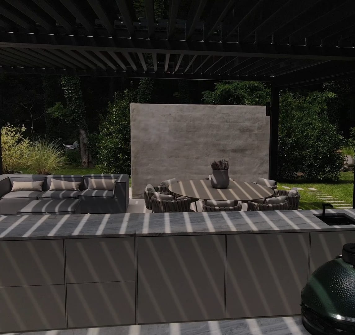 A FREILUFT kitchen run with a stone worktop in the striped shade of a louvered pergola, with a Big Green Egg in front and a dining table and lounge behind