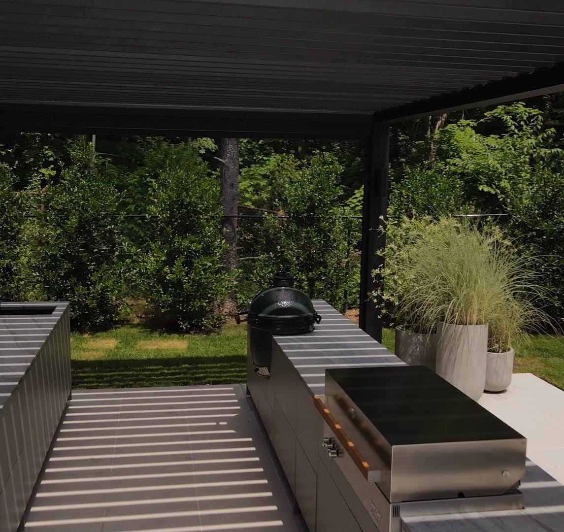 Two FREILUFT kitchen runs facing each other under a louvered pergola, one with a sink, the other with a Big Green Egg and a built-in grill