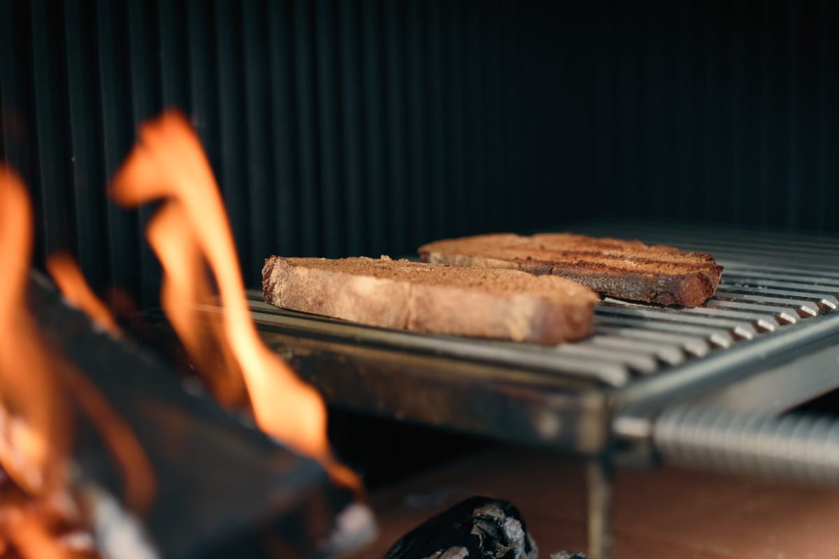Sausages on a stainless grill grate above a burning wood fire