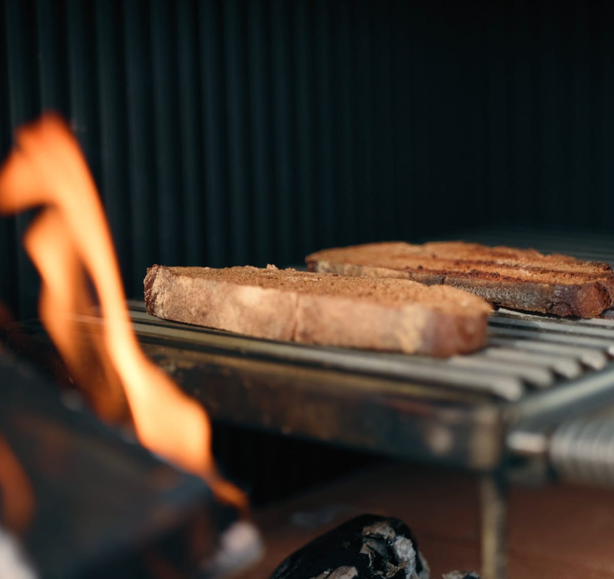 Sausages on a stainless grill grate above a burning wood fire