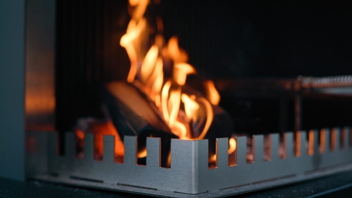 Close-up of a wood fire burning behind the notched steel edge of a FREILUFT grill-and-fire element at dusk