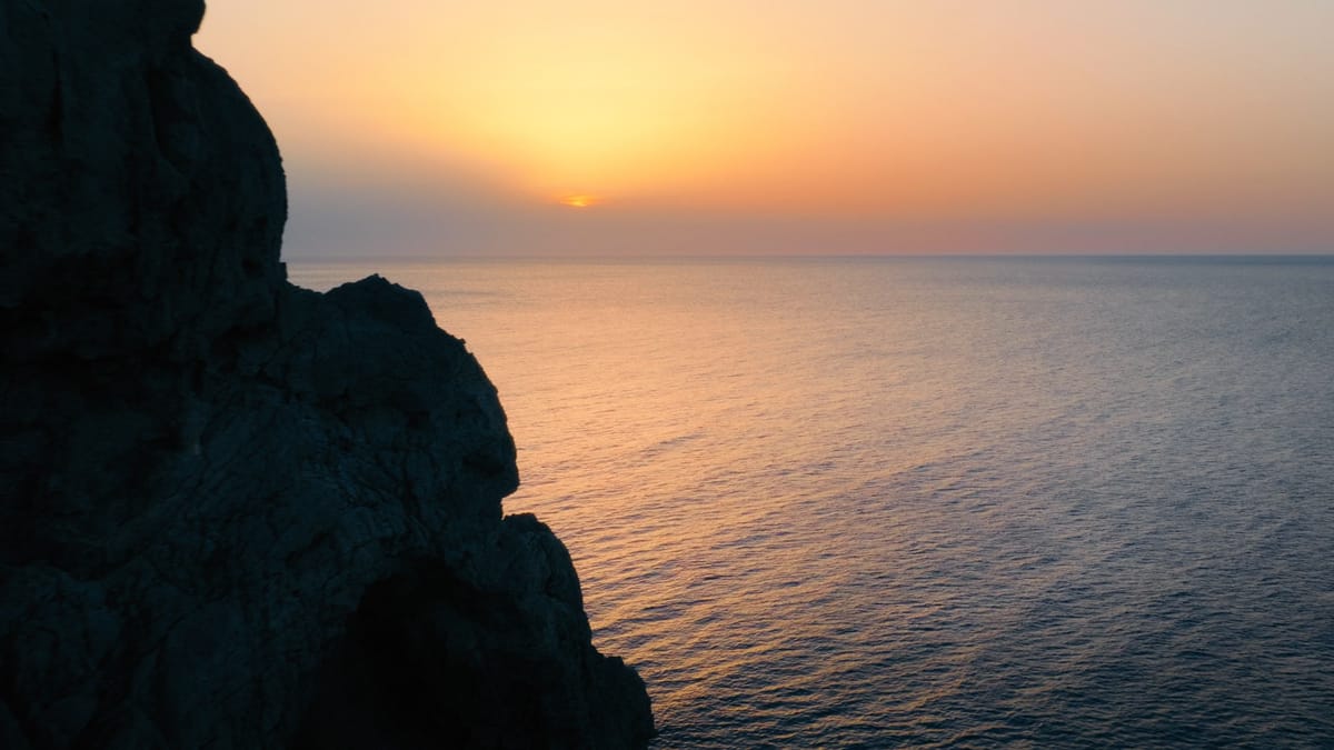 The sun setting over a calm sea beside a rocky coastline