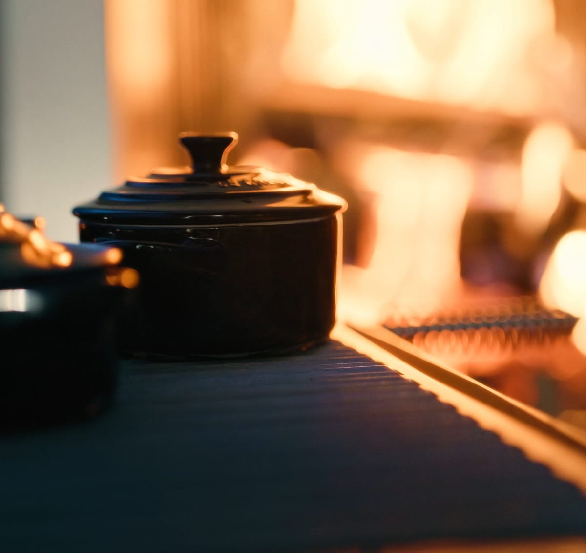 Two black cast-iron pots on a dark stone countertop beside a wood fire