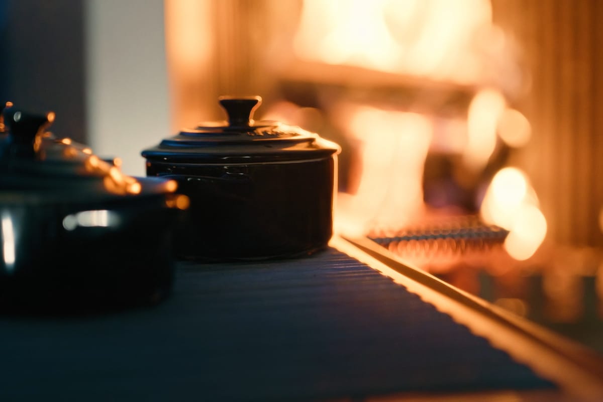 Two black cast-iron pots on a dark stone countertop beside a wood fire