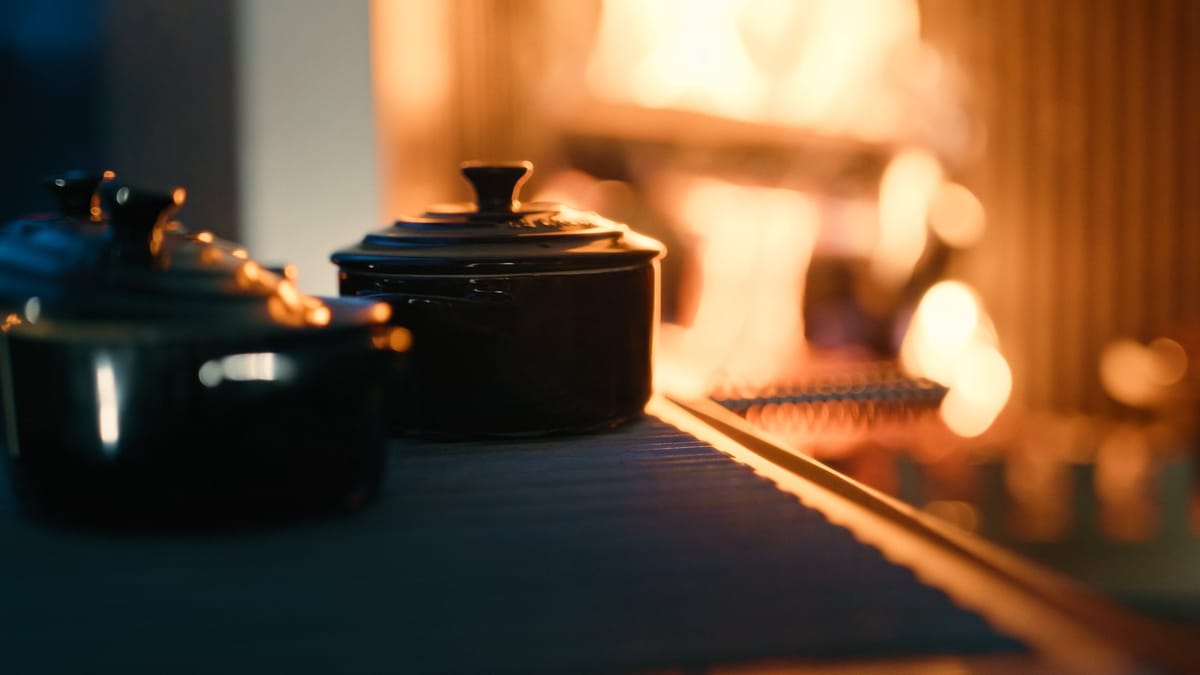 Two black cast-iron pots on a dark stone countertop beside a wood fire